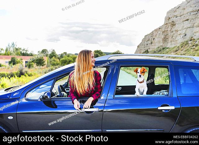 Happy young blond woman and pet dog at car's windows