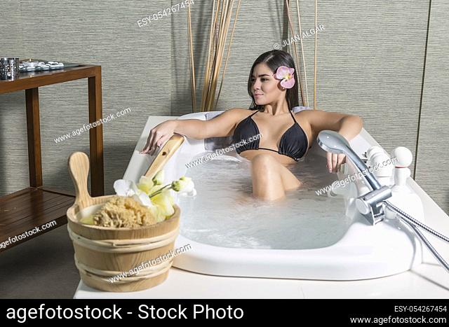 Young beautiful woman with flower in hair lying in hot bath in massage center enjoying health procedure