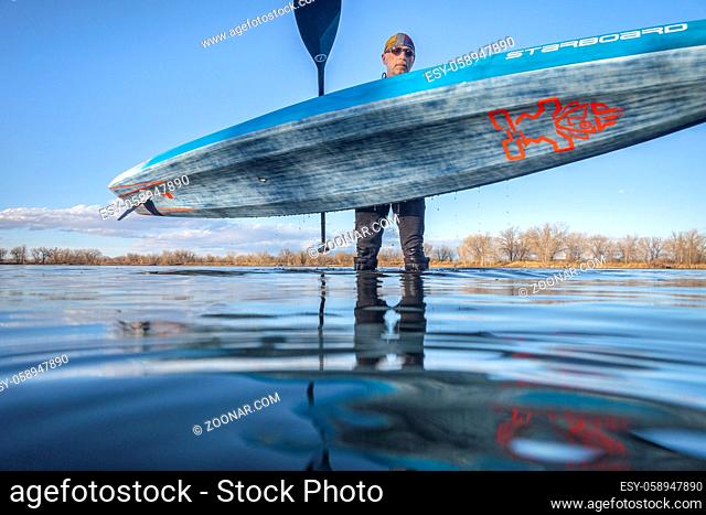 Fort Collins, CO, USA - March 24, 2020: A senior male paddler is carrying Starboard racing stand up paddleboard after paddling training