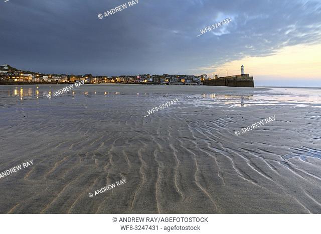 Smeatons Pier and the harbour front at St Ives on the North coast of Cornwall, captured with sand ripples in the foreground during twilight on a morning in...