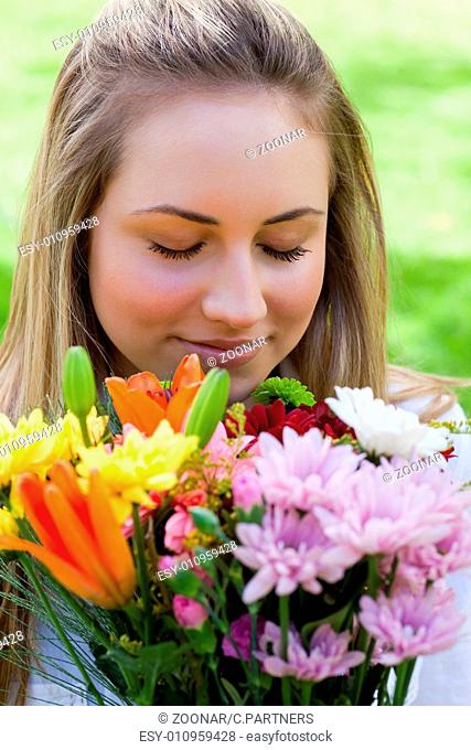 Young blonde girl closing her eyes while smelling a bunch of flowers