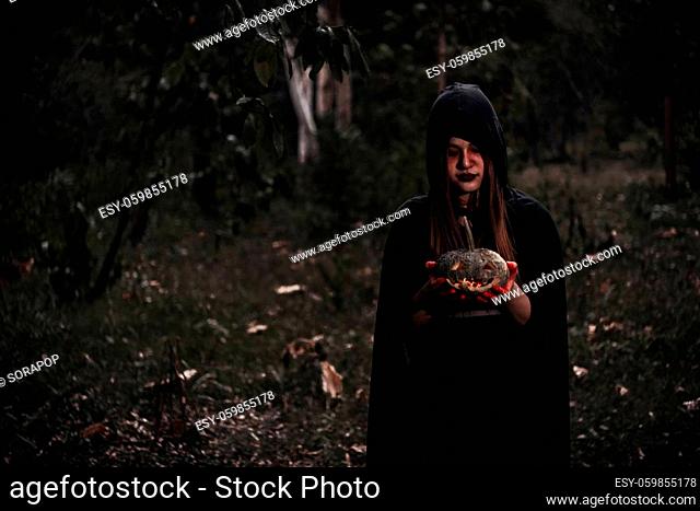 Woman horror ghost holding reaper and pumpkin inn forest, halloween concept