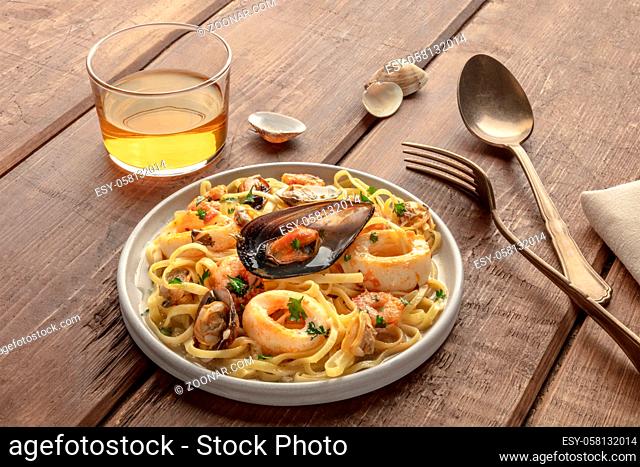 Seafood pasta. Tagliolini with mussels, shrimps, clams and squid rings, with a glass of wine on a dark rustic wooden background