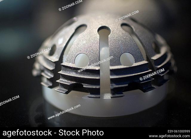 Closeup macro photograph of traumatology and orthopedic surgery metal hip ball joint implant with screw holes and screws against plain background defocused