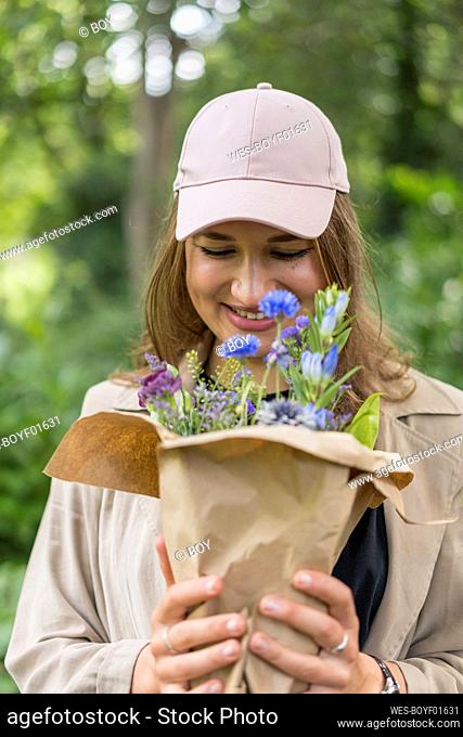 Beautiful young woman smiling while looking at bunch of flower while standing in park