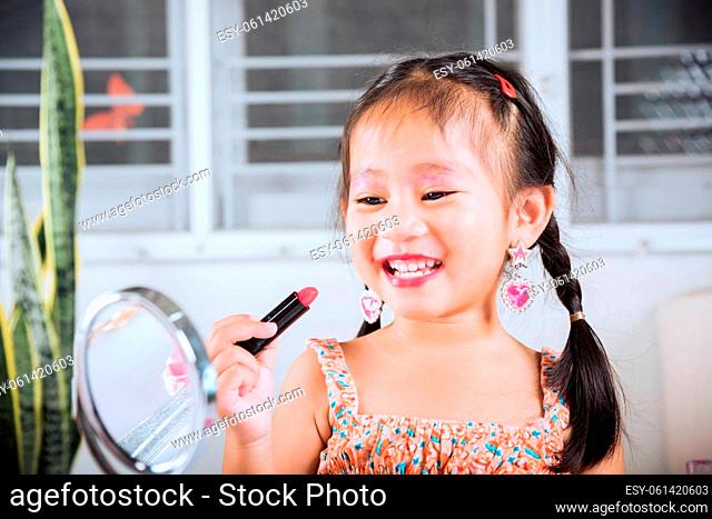 Happy kid is beautiful make up with cosmetics toy, Asian adorable funny little girl making makeup her face she looking in the mirror and applying red lipstick...