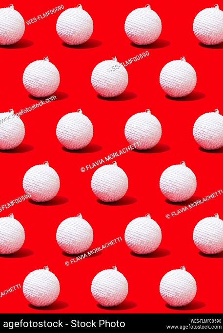 Pattern of white-colored Christmas ornaments flat laid against vibrant red background