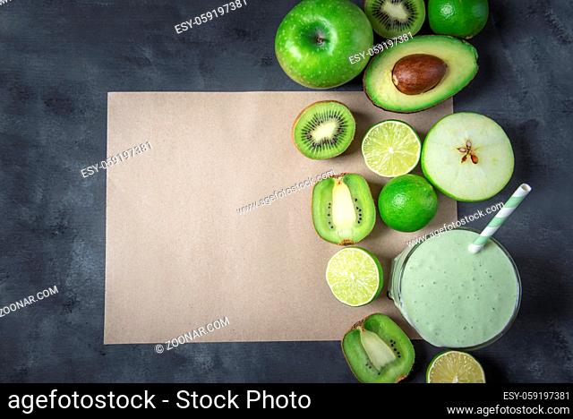Green fruits and a glass with a smoothie, on an empty brown paper page, on a greyish background. Detox drink. Dieting context. Healthy eating