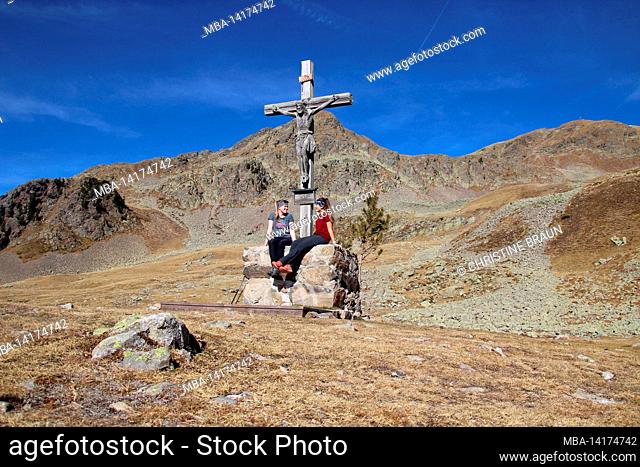 Two young women take a break on a hike. Latzfons, Klausen, Bolzano Province, South Tyrol, Italy, Europe. The shelter and the pilgrimage church Latzfonser Kreuz