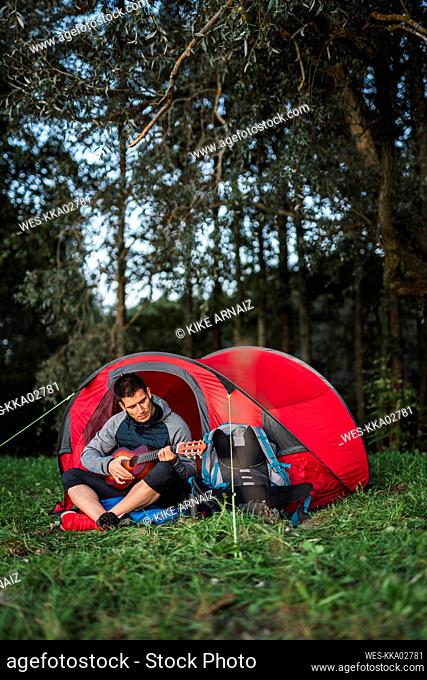 Man camping in Estonia, sitting in his tent, playing the ukulele