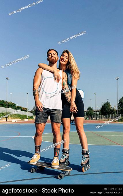 Smiling young couple holding hands at basketball court on sunny day
