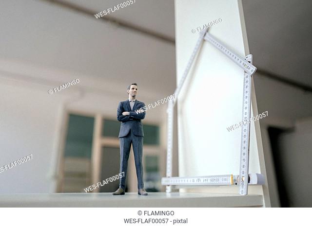 Businessman figurine standing on table with pocket rule, shaping a house