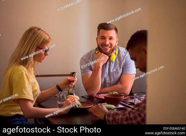 Happy friends spending their free time in vegan restaurant or cafe. Smiling man looking at camera while his friends eating healthy vegan dishes