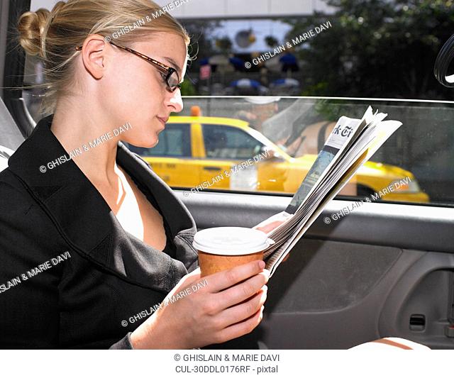 Business woman reading news paper in cab
