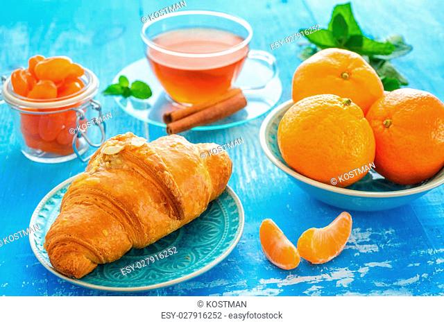 cup of tea, croissant, and mandarines on blue background
