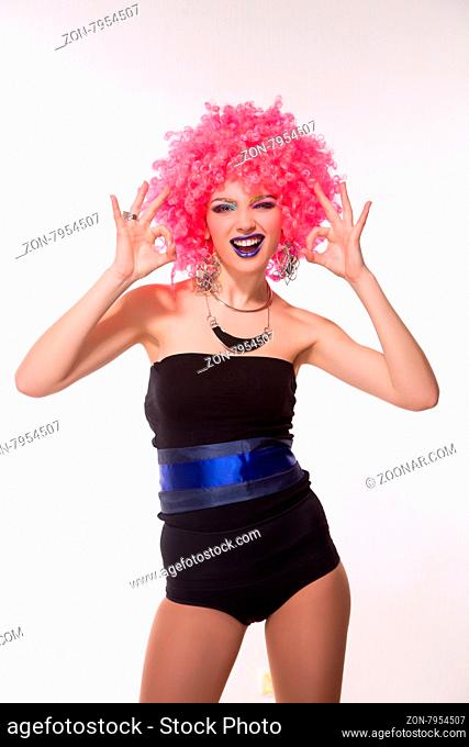 Portrait of beautiful party girl in pink wig showing okay sign with both hand. Happy lady smiling in photo studio isolated on white background