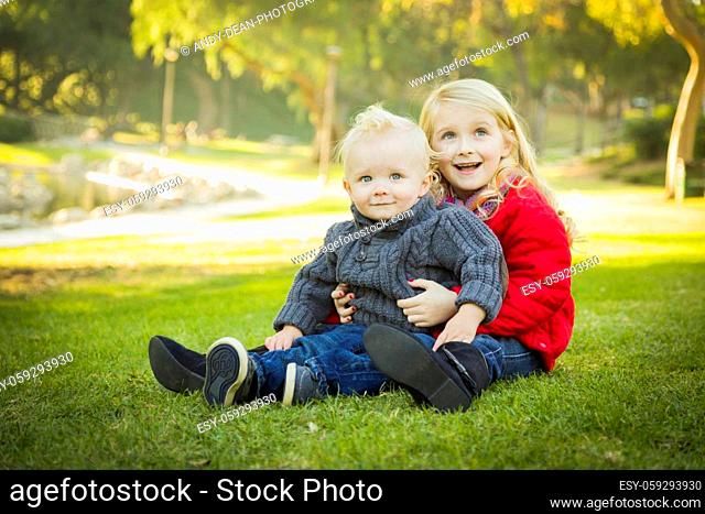 Little Girl with Her Baby Brother Wearing Winter Coats Outdoors Sitting at the Park.