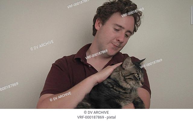 A man holds and pets a striped cat