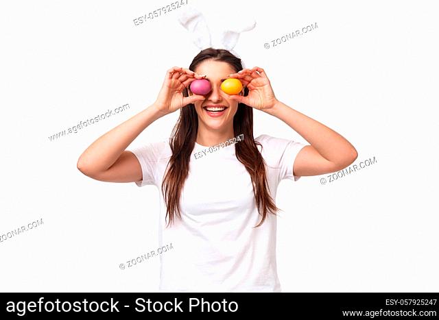 Portrait of funny and carefree cute young girl in rabbit ears, making eyes from colored eggs, celebrating Easter day, having fun