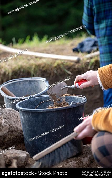 PRODUCTION - 18 October 2023, Bavaria, Friesen: Earth falls from a trowel into a bucket. Volunteers from the Kronach Archaeological Working Group uncover stone...