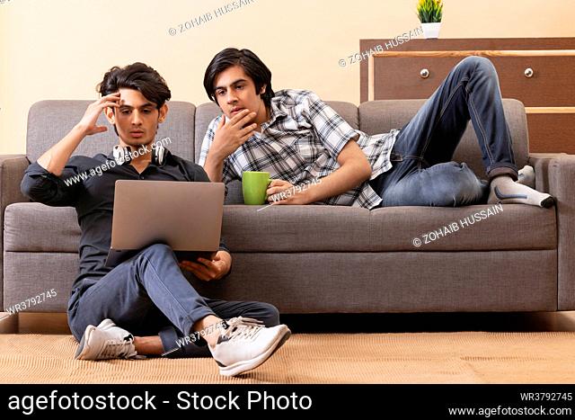 Teenage boys using laptop together while sitting on floor in living room
