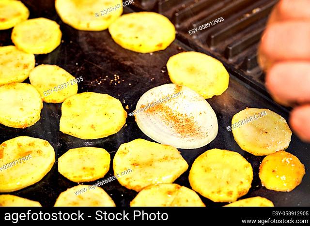 Slices potatoes and onion seasoned with spice grilled on electric grill, closeup photo