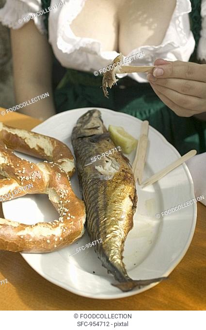 Woman eating Steckerlfisch skewered fish with pretzel, Oktoberfest