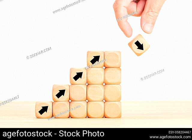 Hand and wooden block with falling arrow. Stock market collapse or financial economy crisis concept. Business uncertainty concept and risk idea
