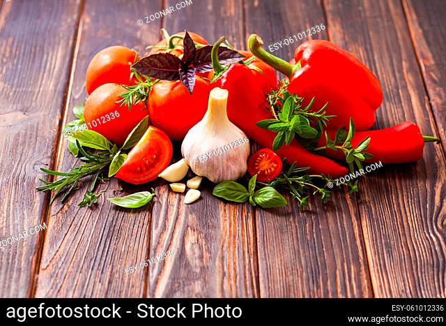 Fresh vegetables with various aromatic herbs on a wooden table. Tomatoes, peppers and garlic with italian herbs