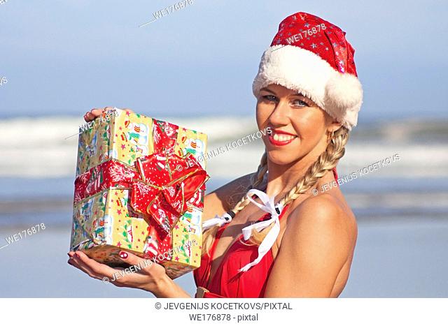 Santa girl in Santa dress with Christmas gift on the beach