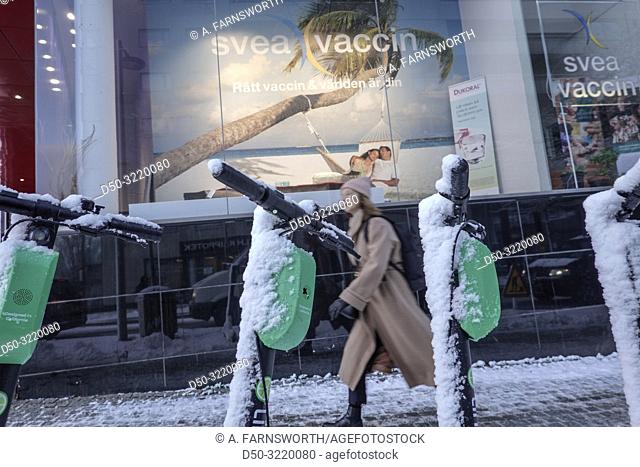 Stockholm, Sweden A young woman walks by an advertisement in the snow for a store selling vaccines for travelers in Liljeholmen