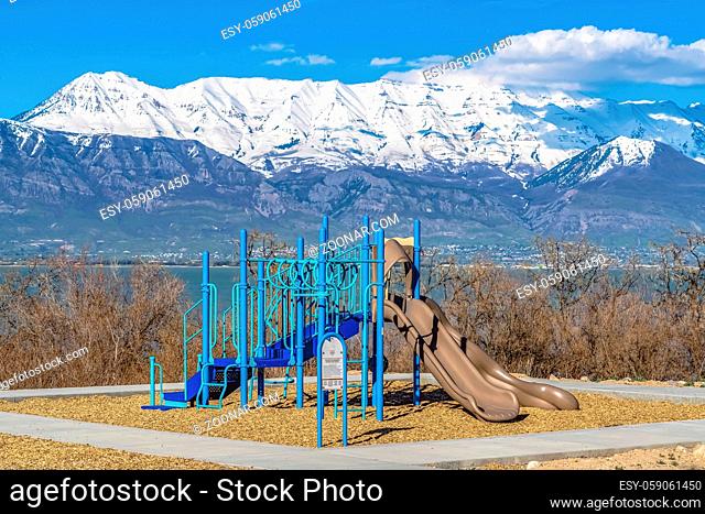 Playground with view of lake and snow capped mountain on a sunny day. Residential area near the base of the mountain can be seen beyond the calm water