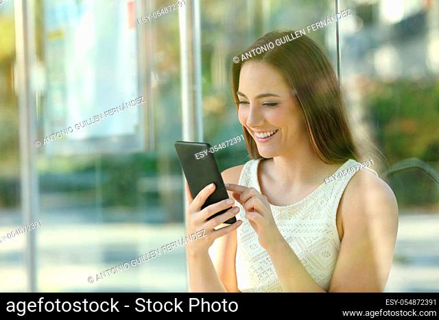 Happy young woman checking smart phone waiting for the bus to come