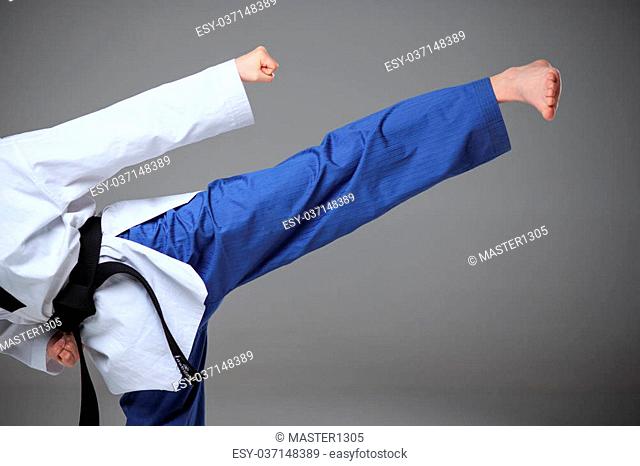 The hand and foot of karate girl in white kimono and black belt training karate over gray background