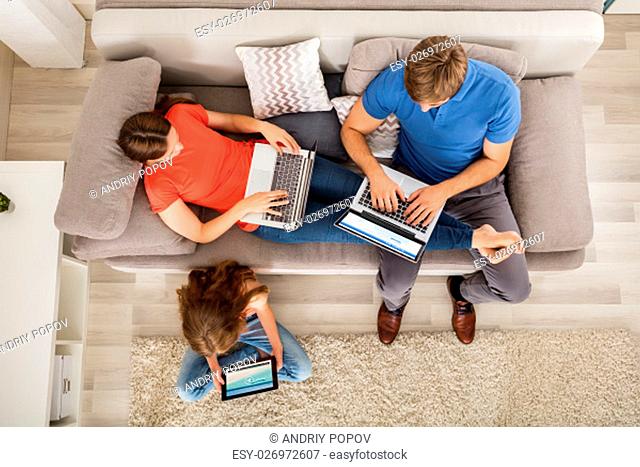 Girl Watching Video On Digital Tablet While Her Parent Working On Laptop