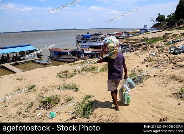 PRODUCTION - 08 November 2023, Brazil, Parintins: A man carries bags of food to a boat. The drought in the Amazon region is causing difficulties in everyday...