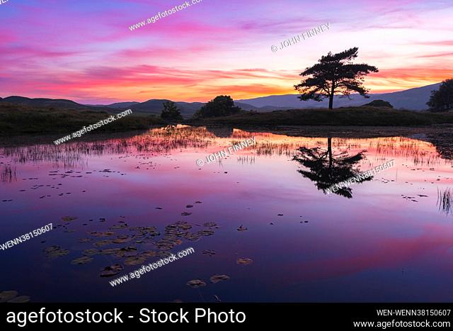 Vivid colours across the sky at dusk reflect on the water at Kelly Hall Tarn near the village of Torver and Coniston Water in Cumbria