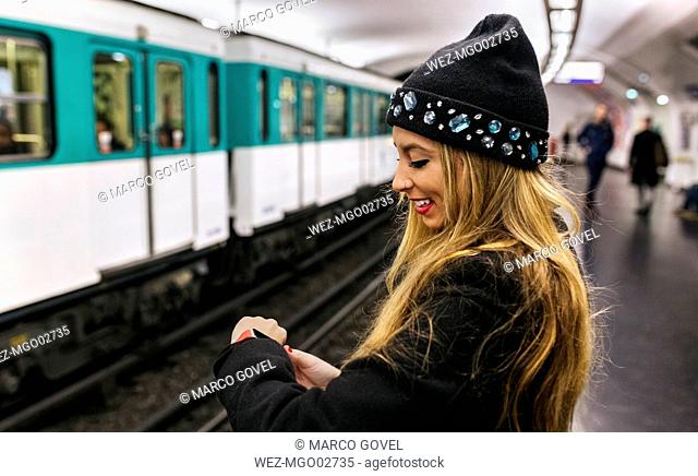 Paris, France, young woman looking at her smartwatch at underground station platform