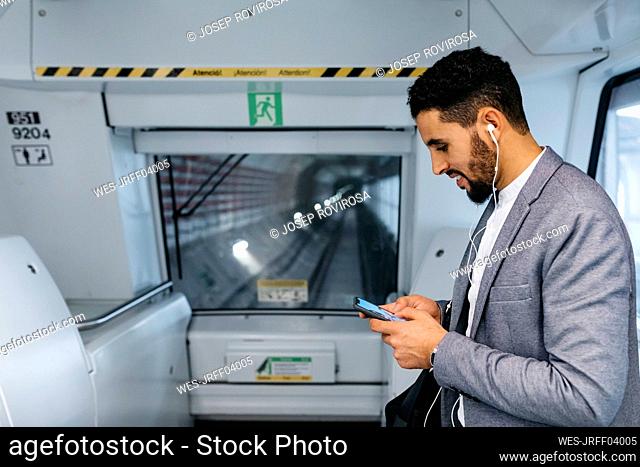 Young businessman with cell phone and earphones on the subway