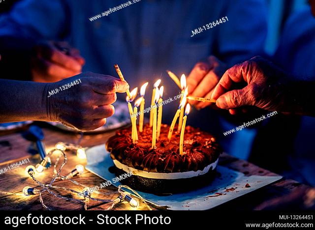 Close up of people hands fire candles on a birthday celebration cake on the table - concept of event and people have fun together in friendship or family...