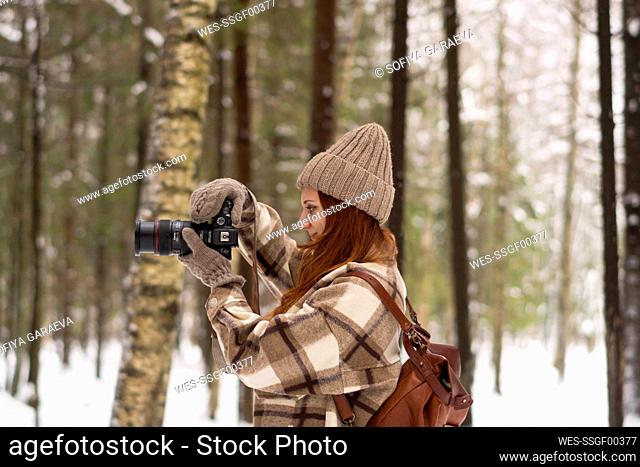 Mujer fotografiando con cámara en el bosque en vacaciones de invierno