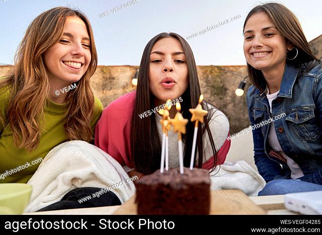 Young woman with female friends blowing candles on birthday
