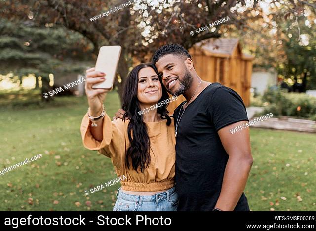 Smiling woman taking selfie with man through mobile phone while standing at backyard