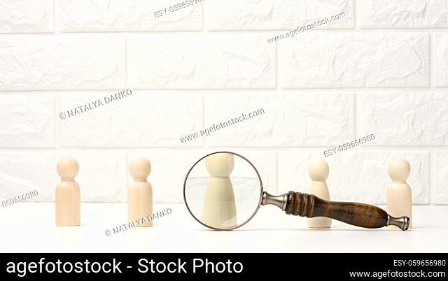 wooden figures of men stand on a white background and a magnifying glass. Recruitment concept, search for talented and capable employees, career growth