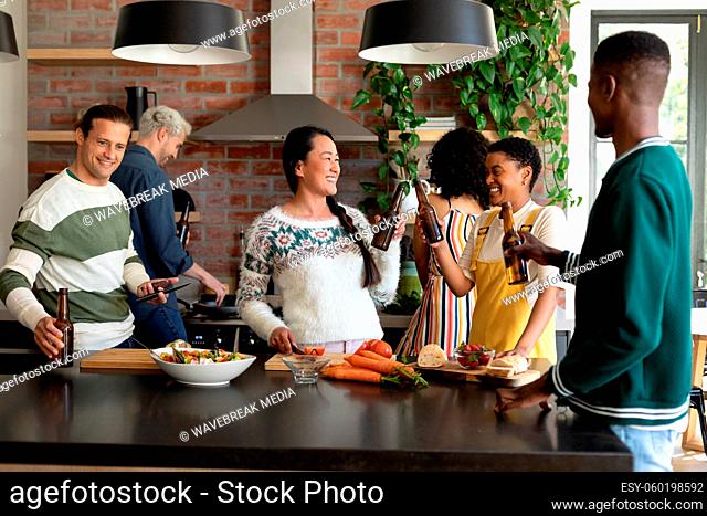 Group of happy diverse female and male friends drinking beer and cooking together in kitchen
