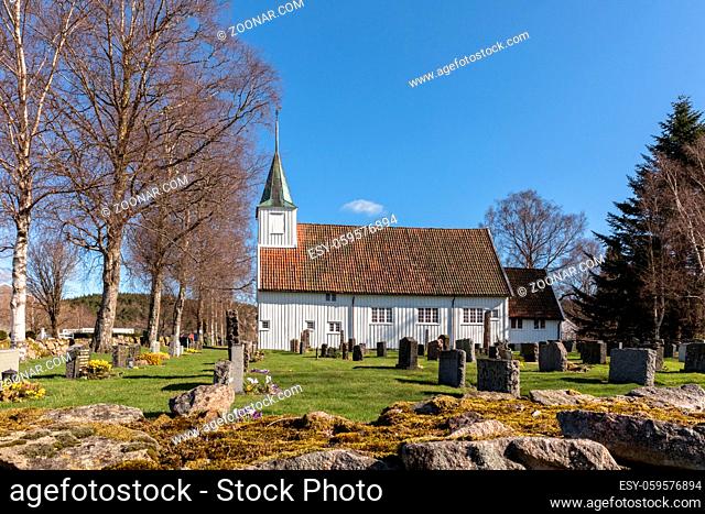 White wooden church in Sogne, Vest-Agder in Norway. Blue sky, green grass. Buildt around 1640