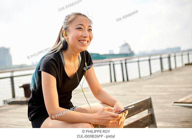 Woman wearing earphones holding smartphone smiling