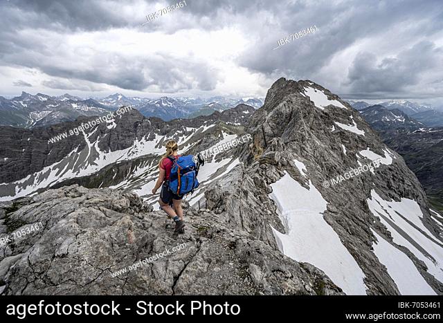 Hiker, mountaineer on ridge trail with remnants of snow, mountain panorama with summit high light, dramatic cloudy sky, Heilbronner Weg, Allgäu Alps, Allgäu