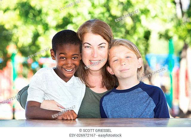 Mother hugging and sitting in between adopted child and son at table in park