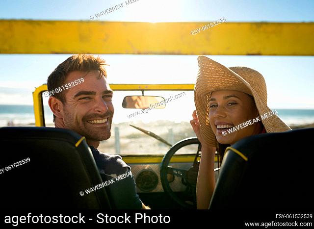 Happy caucasian couple sitting in beach buggy by the sea looking to camera
